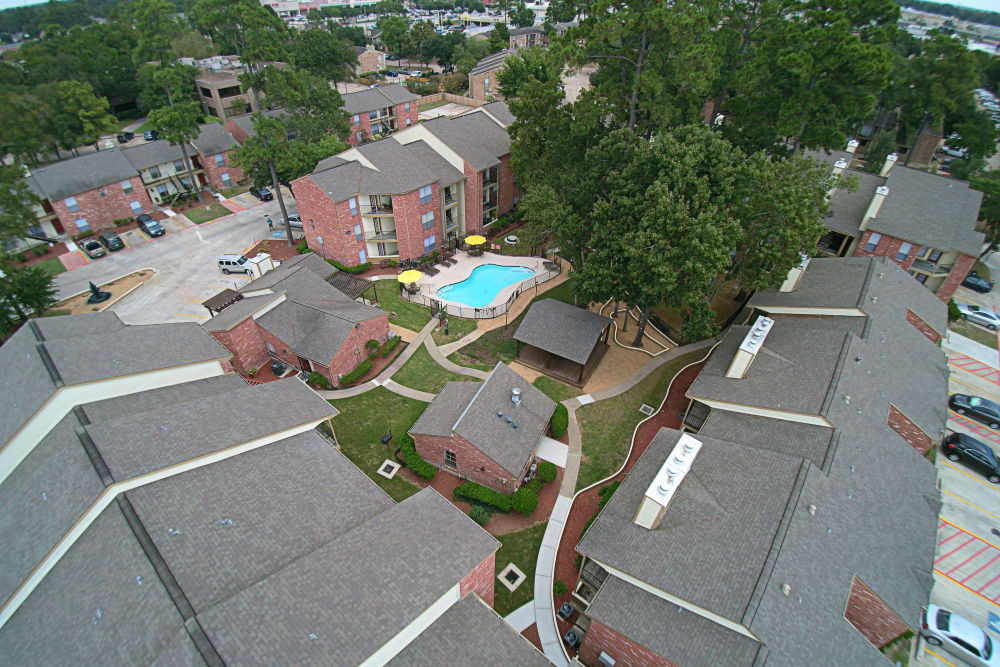 Aerial view of Deerbrook Apartments with green grass, blue pool, and tall green trees around the paths.