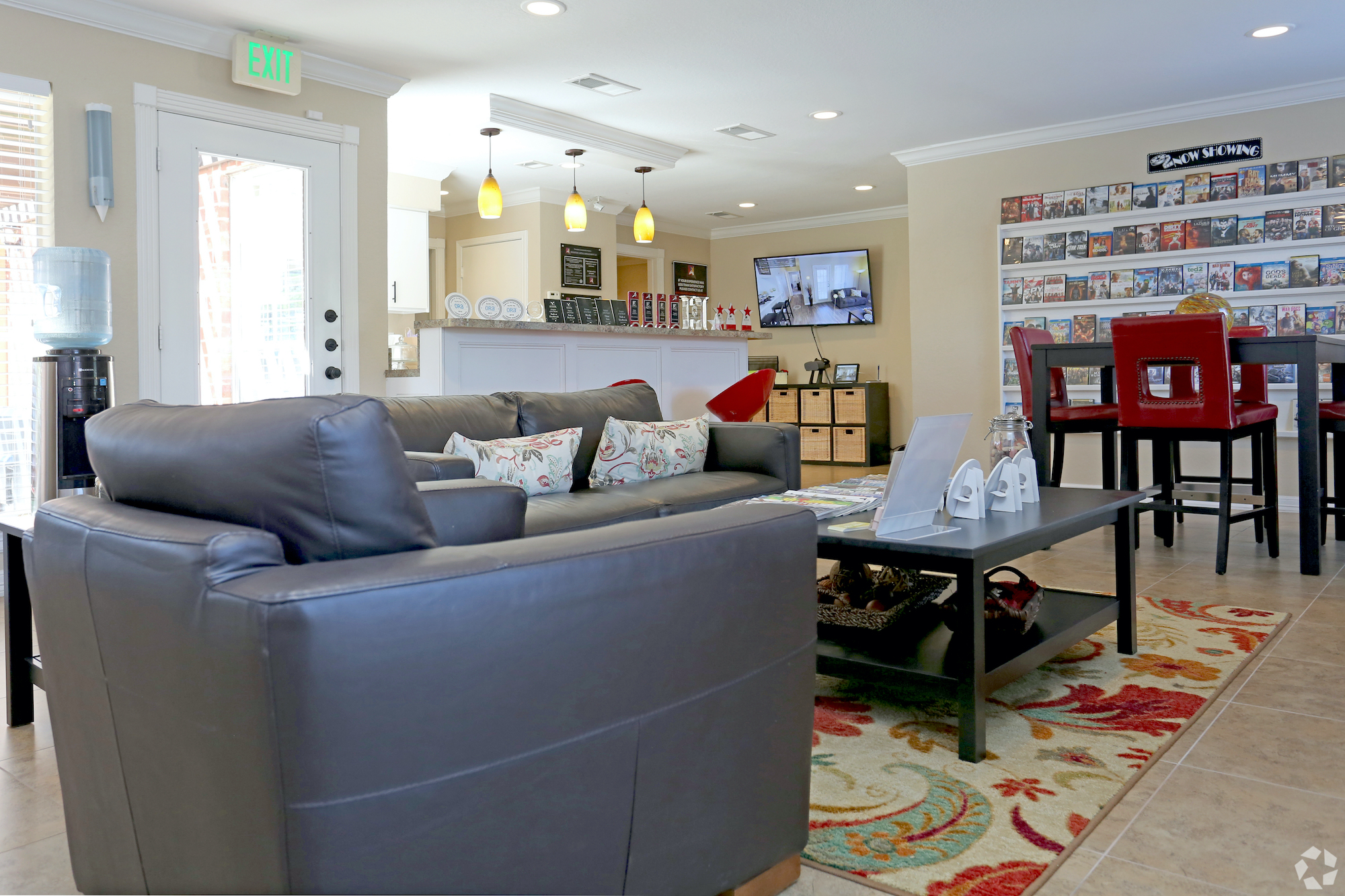 Community lounge at Deerbrook Apartments. Two gray leather couches, a dark wood coffee table, tall dark wood dining table and kitchenette in the background.