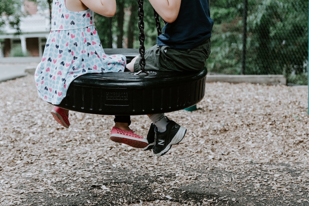 Two kids playing on a tire swing.