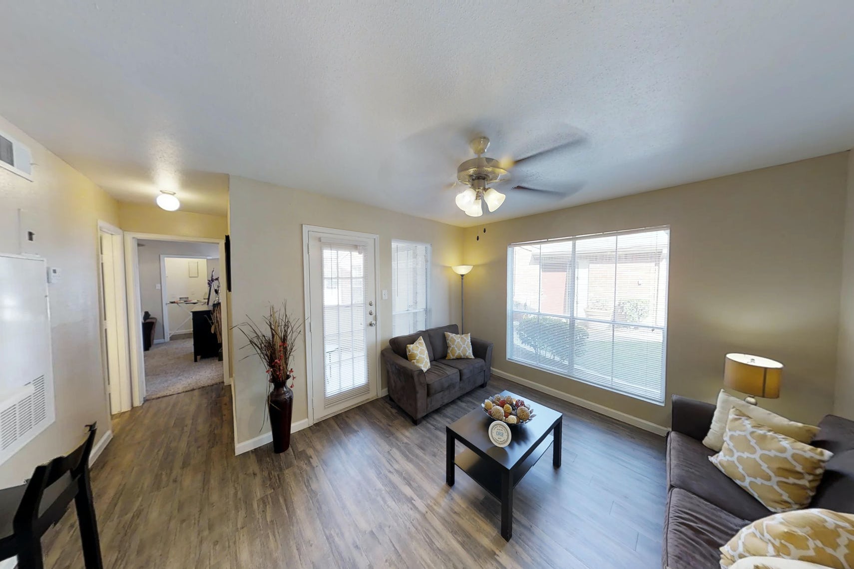 Living space at Deerbrook Apartments with two windows, a door to ouside, and a hallway leading to the bedroom.